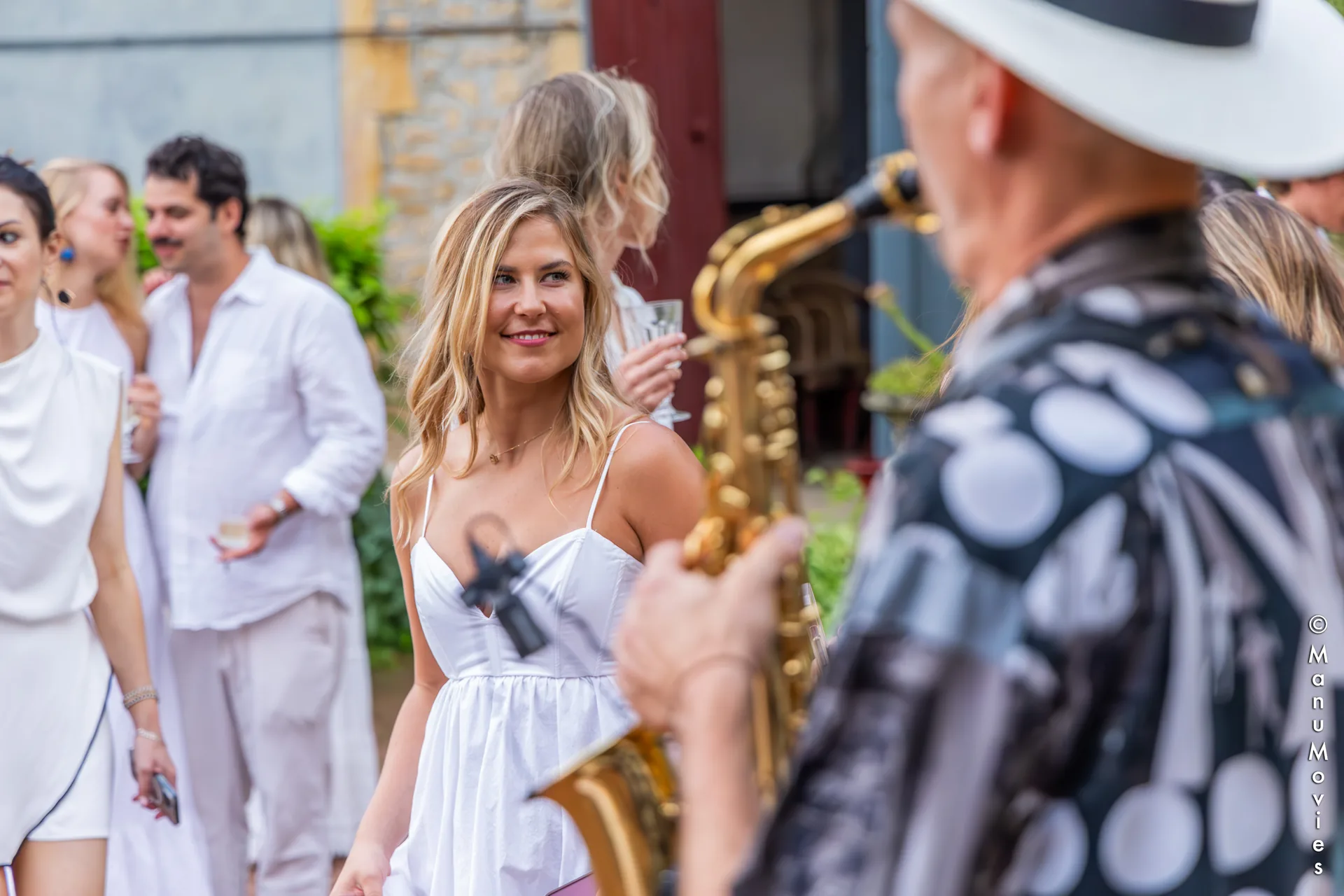 Golden saxophone in the foreground at an all-white party, a guest in a white dress smiling